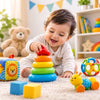 A smiling baby in a cream outfit crawls on a carpet while stacking colorful ring toys. The scene is a bright, playful nursery with a teddy bear, shelves, and other toys visible in the background.