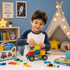 Young boy in a navy and white shirt smiling while building a colorful toy vehicle with interlocking blocks on a table. BUILD & PLAY toy set box visible nearby, with a cozy room, teepee, bookshelves, and educational toys in the background.